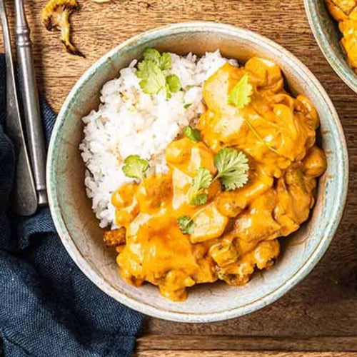 A bowl of Aloo Gobi with white rice, garnished with cilantro, arranged on a rustic wooden table 