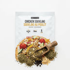 A package of Epicure Chicken Souvlaki seasoning mix, shown on a clean white background with the seasoning spilled out below in a wooden scoop and pile.