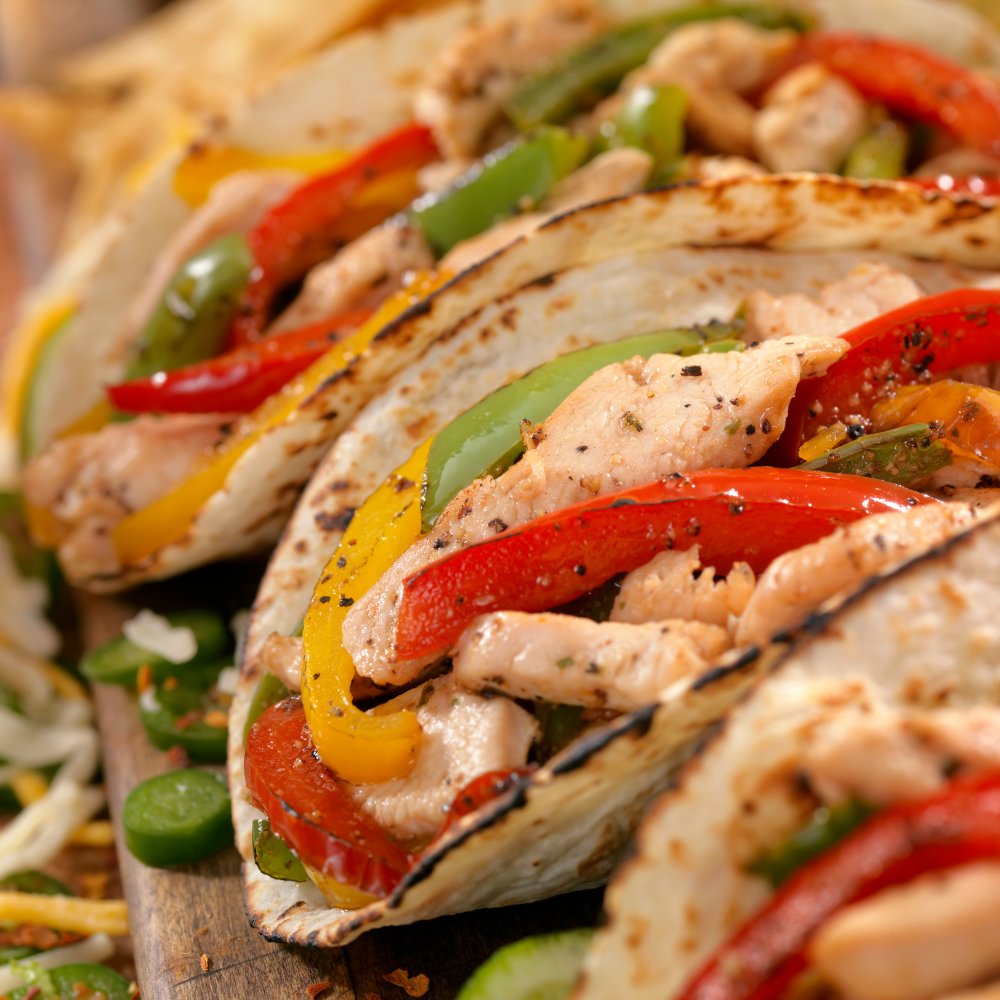 Close-up of three grilled chicken fajita wraps filled with red, yellow, and green bell peppers, served on a wooden board with additional garnish.