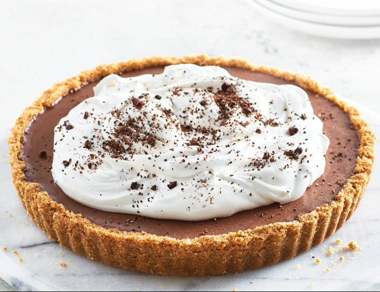 Epicure Chocolate Mud Pie in a graham cracker crust topped with whipped cream and chocolate cookie crumbles on a white plate