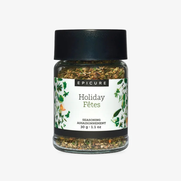 A jar of Epicure Holiday Fêtes seasoning with a black lid and a white label decorated with green leaves and small orange illustrations, set against a plain light gray background.