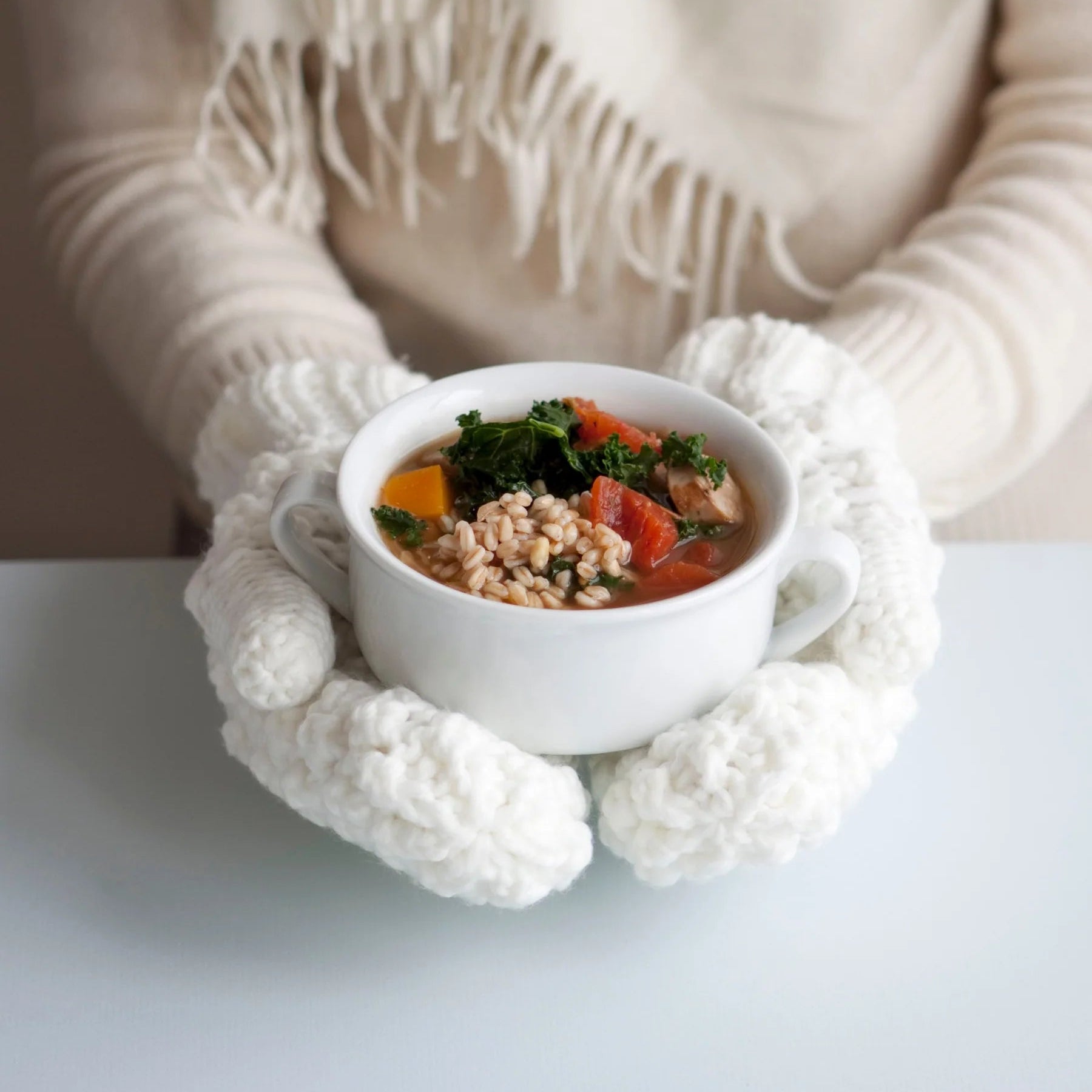 Woman wearing white mittens holding white bowl of soup