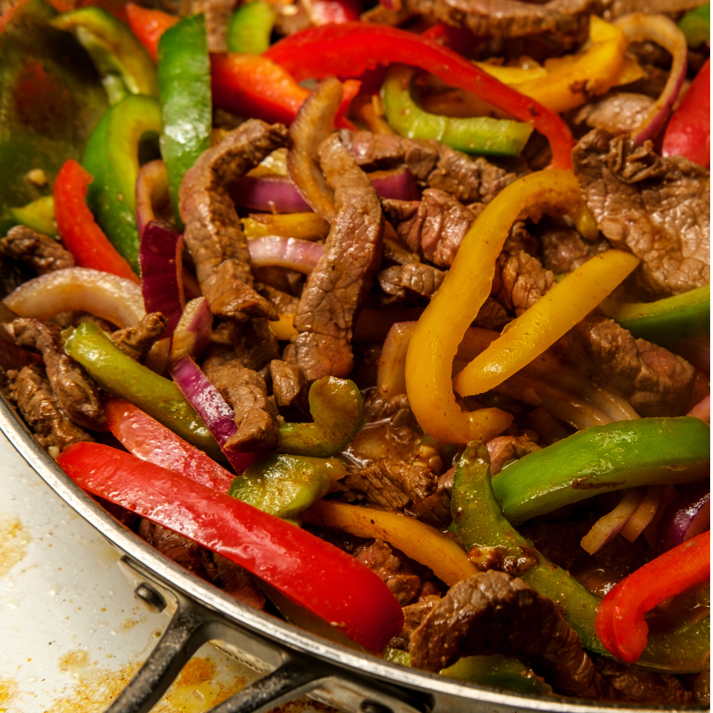 A close-up shot of a pan-fried beef fajita stir-fry with colorful bell peppers and onions in a skillet.