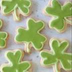 Shamrock-shaped sugar cookies decorated with light green icing, arranged on a light marble surface.
