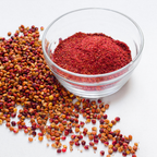 A glass bowl filled with ground sumac and a pile of sumac berries spilled on the side.