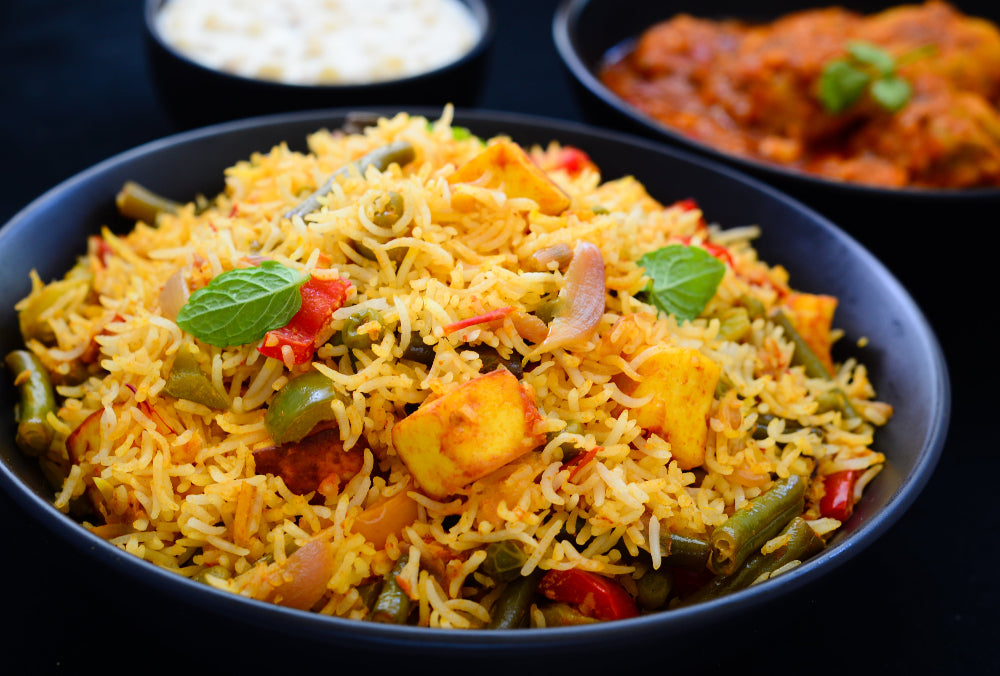 Blue bowl of vegetable biryani with tofu in foreground.