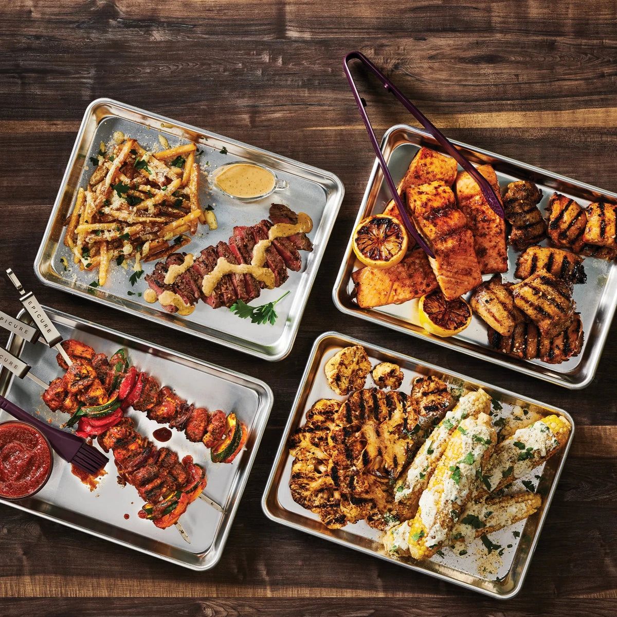 Four trays of grilled and roasted meats and vegetables on a wooden surface, seasoned with Epicure BBQ Chicken & Rib Rub