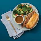Plate with beef on a bun, salad, and dipping sauce on a blue background