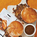 Beef on a bun with beef dip on a wooden board on an orange textured background