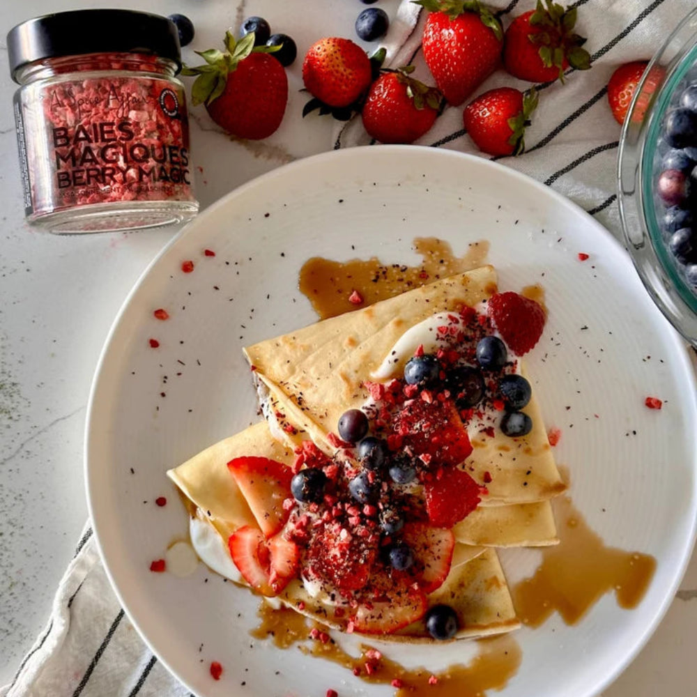 Crepes with berries and a jar of A Spice Affair Berry Magic on a white plate on a white table with loose berries 