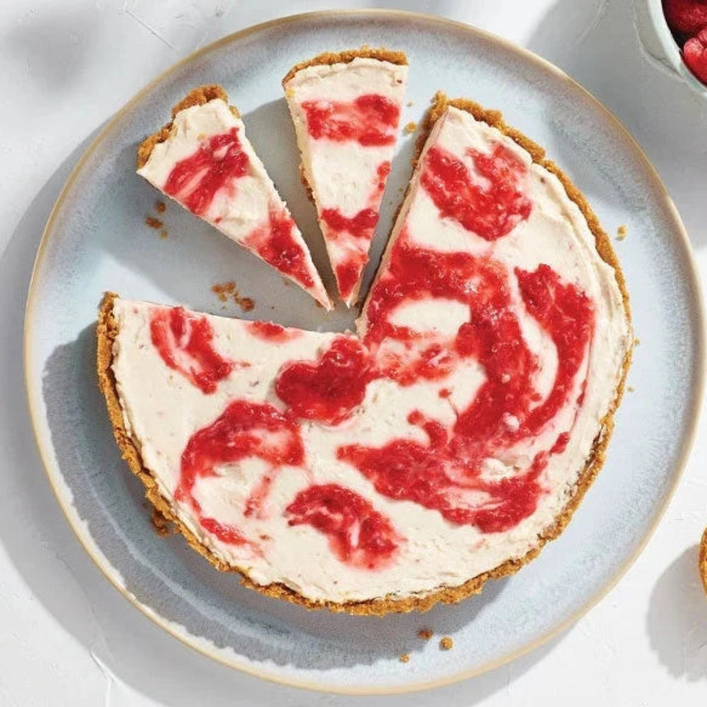 Epicure Berry Swirl No-Bake Cheesecake Mix featuring a creamy raspberry-swirled cheesecake on a plate, sliced into wedges with fresh raspberries and a mini tart nearby