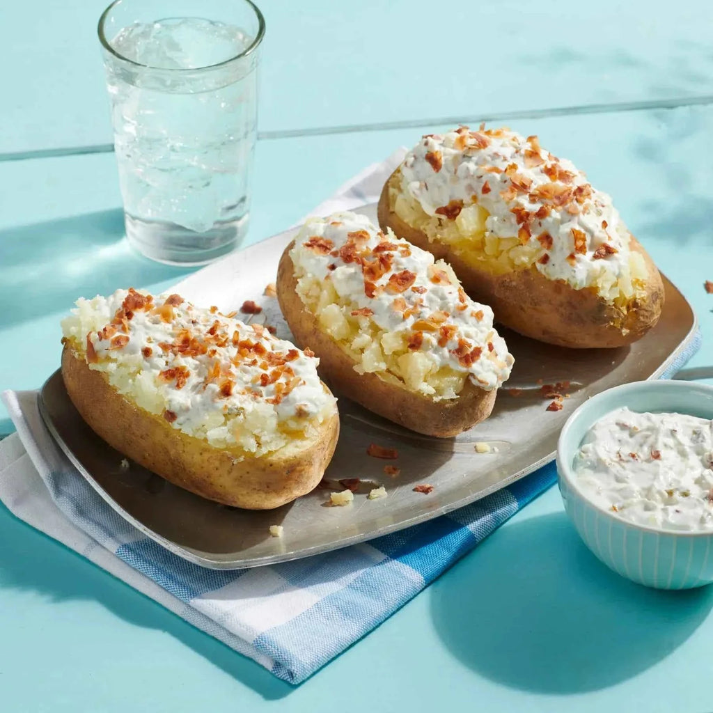 Three baked potatoes with toppings on a plate with a glass of water and a bowl of sour cream on a light blue background.