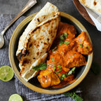 Butter Chicken Seasoning with creamy tomato chicken curry garnished with cilantro and mint alongside toasted naan and lime on a dark table