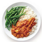  A white plate containing a serving of butter chicken on white rice with green beans on the side sitting on a white background.