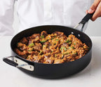 Person holding a black frying pan with a cooked dish of Carne Guisada on a white surface.