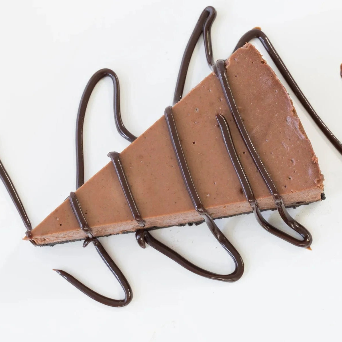 Chocolate Velvet Cheesecake slice topped with rich chocolate drizzle on a white plate with a fresh raspberry garnish‑