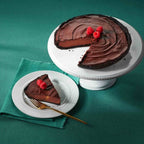 Chocolate Velvet Cheesecake topped with raspberries on a white cake stand alongside a plated slice with fork on a teal cloth