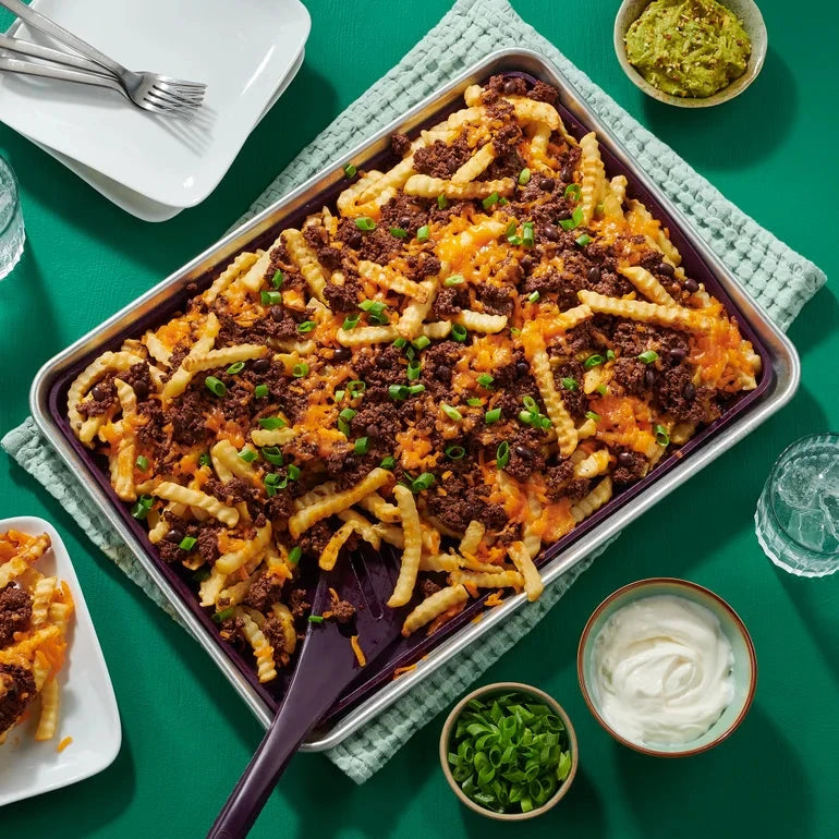 Tray of loaded fries with chili and cheese on a green table with side dishes.