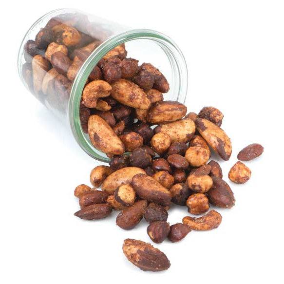 Crispy roasted almonds and cashews spilling out of a clear glass jar on a solid white background.