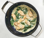 Skillet with creamy sauce, chicken, and spinach on a white background