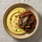 Overhead view of a ceramic bowl filled with creamy yellow polenta and a ragu  topped with parsley and shredded cheese, set on a textured light beige linen surface.