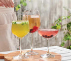 Three glasses of colourful cold herbal teas on a wooden board with a blurred outdoor background