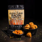 A package of 'Everything Bacon Partout' vegan and vegan-friendly bacon balls by 'A Spice Affair' is displayed on a black stand. The packaging is black and tan with orange accents.