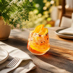Fizzy Pink Sangria Mix served as a sparkling pink-orange drink with orange slices and berries in a glass on a rustic table beside place settings and flowers