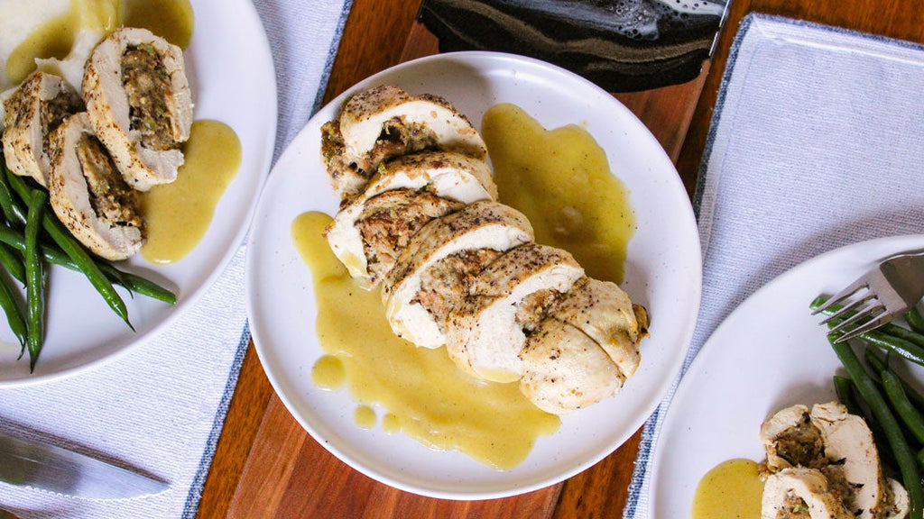 Sliced stuffed chicken breast with a chicken gravy on a white plate, served with green beans on a wooden table.