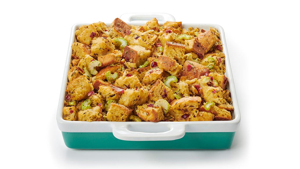 A square baking dish filled with stuffing, photographed on a clean white background. The dish has a white top and handle area with a teal-green base.