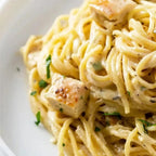 A close up view of a serving of herb and oil pasta with chicken on a white plate