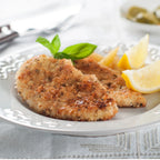 Breaded cutlet dish on a plate with lemon wedges and basil leaves.