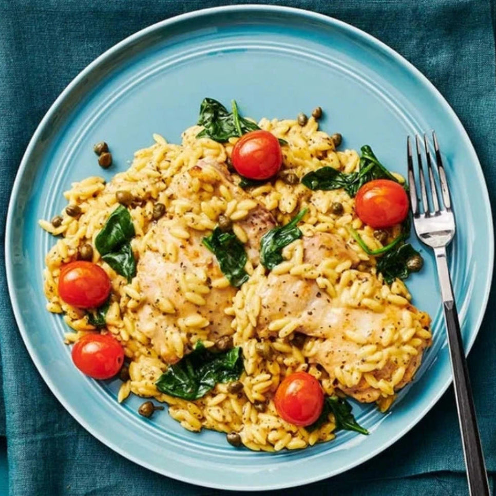 Orzo pasta with chicken and cherry tomatoes on a blue plate with a fork on a blue tablecover