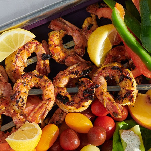 Grilled Lemon Pepper shrimp skewers with lemon slices and colorful vegetables in a metal tray.