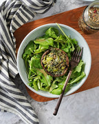 Maple & Pepper Seasoning sprinkled over a stuffed mushroom on fresh green salad, with the seasoning jar and fork arranged on a wooden board