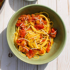Green bowl of spaghetti with tomato sauce and cheese on a wooden surface