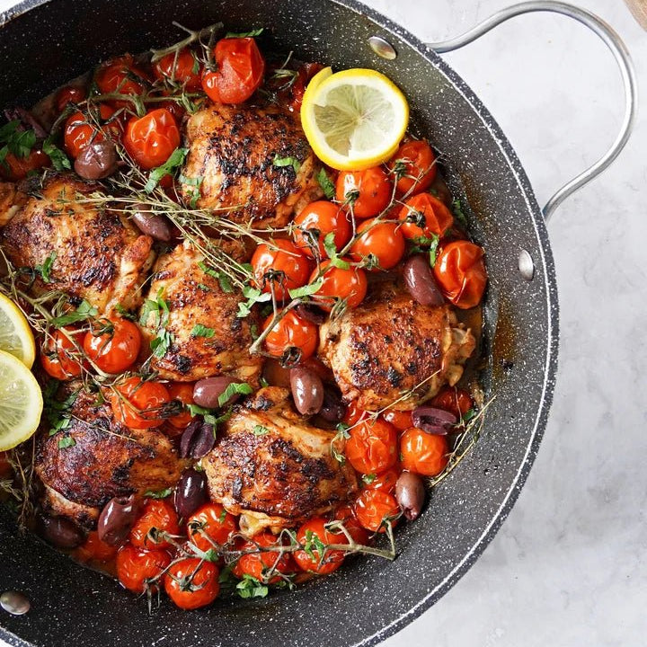Mediterranean Chicken with cherry tomatoes in a skillet with lemon slices on a white marble top