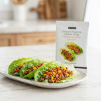 Three lettuce wraps filled with ground meat and colorful vegetables are served on a white plate, with a package of Epicure Crispy & Crunchy Lettuce Wrap seasoning standing behind them on a light countertop.