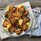 Plated chicken dish with lemon wedges and thyme on a wooden table.