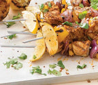 Grilled skewers with Piri Piri chicken, vegetables, and lemon wedges on a white surface.