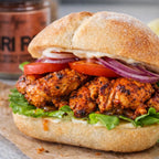 Piri Piri Spices chicken sandwich on a toasted bun with crisp lettuce tomato red onion and creamy sauce close up beside a spice jar