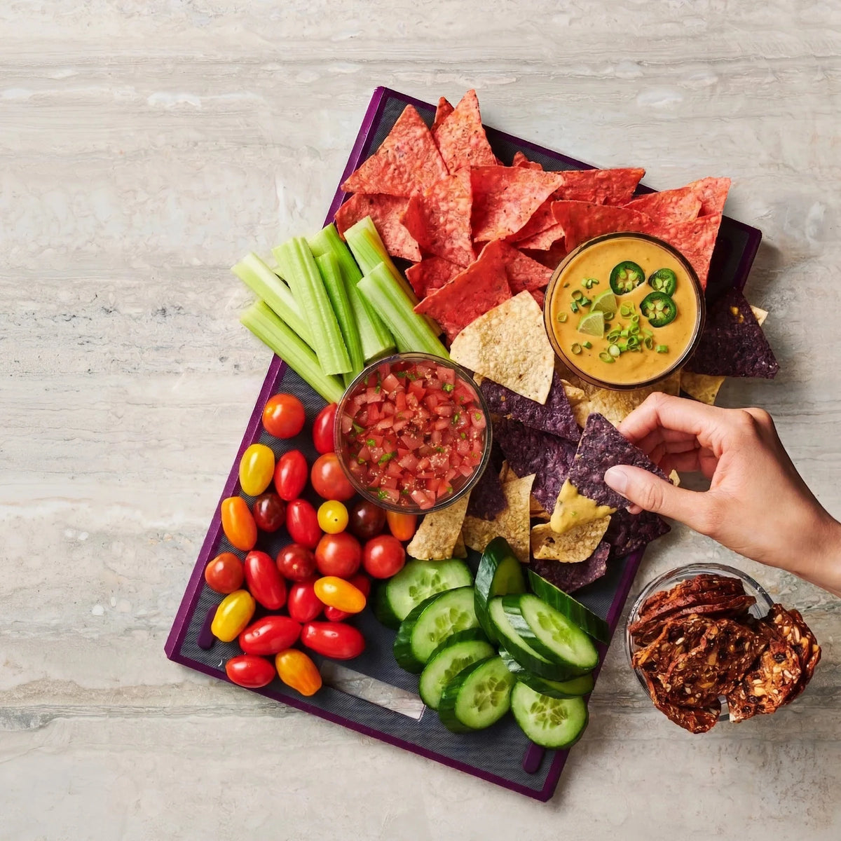 Ooey Gooey Queso Hot Dip Mix with creamy queso dip, tortilla chips, celery, tomatoes, cucumbers, salsa, and a hand dipping a chip on a serving board