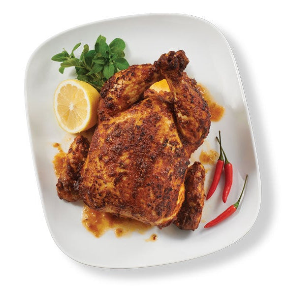 A whole roasted chicken with a Portuguese Chicken Seasoning, served on a white square plate with a lemon wedge, green herbs, and two red chili peppers, isolated on a white background.