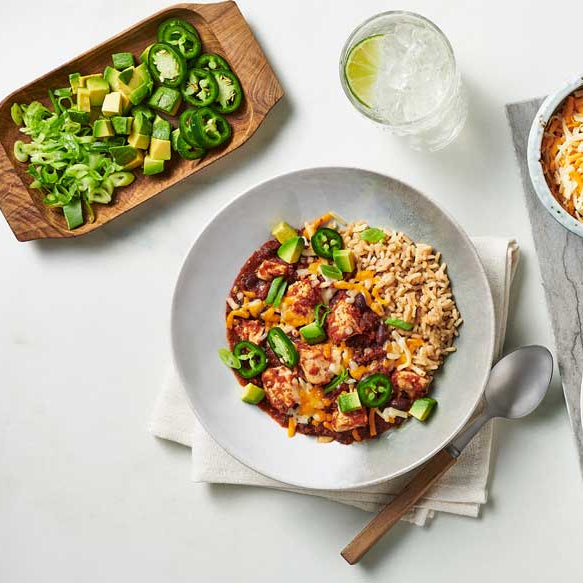 Chicken Ranchero Skillet with jalapeños, avocado and scallions, served on a white table with side dishes and utensils