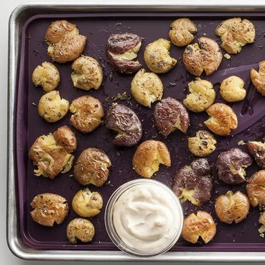 Roasted seasoned potatoes on a baking tray with a small bowl of cream sauce.