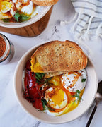Roasted Garlic & Sun Dried Tomato Seasoning beside a bowl of eggs with roasted red peppers dill and toasted bread on a marble table