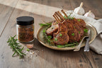 Rack of lamb with herbs on a plate next to a jar of A Spice Affair Savoury Lamb Rub on a wooden table.