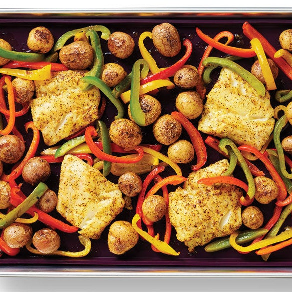 Overhead view of Sheet Pan Lemon Pepper Fish, featuring four pieces of seasoned fish or chicken, small brown potatoes, and sliced red, green, and yellow bell peppers on a white background.
