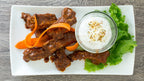 Plated dish of Stampede BBQ Ribs by  Epicure with carrots, lettuce, and a small bowl of sauce on a wooden surface