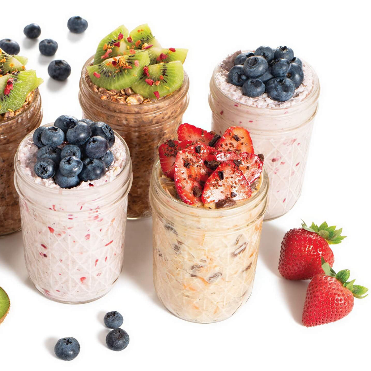 Jars of overnight oats with various toppings including berries and kiwis on a white background